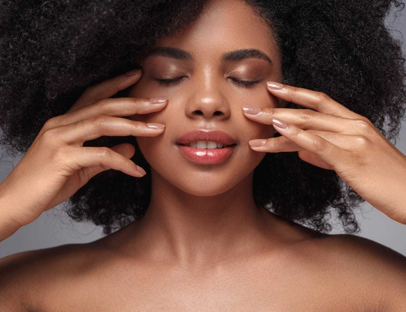 Woman with afro hair enjoying a facial massage with eyes closed.